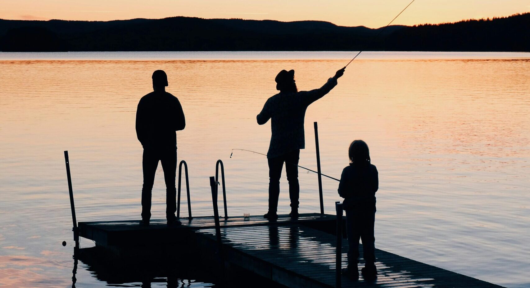 A serene scene of a family fishing together on a lake dock at sunset, creating silhouettes on the water.